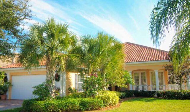 Exterior view of a Florida home with a tile roof, palm trees, and landscaped yard under a blue sky.