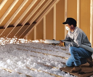 Male worker installing blown-in fiberglass attic insulation.