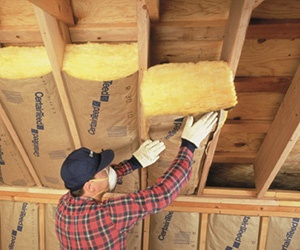 Worker installing kraft-faced fiberglass batt insulation installation in a ceiling.