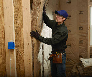 Man installing kraft-faced fiberglass batt insulation in an interior wall.
