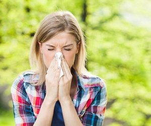 woman blowing nose due to allergies