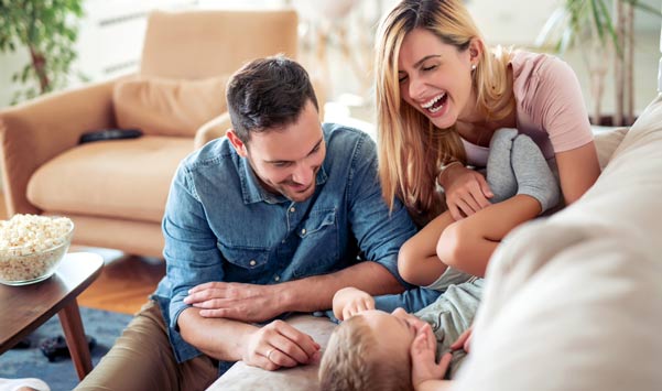 Happy family of three (dad,mom, and toddler) smiling and laughing together on couch.