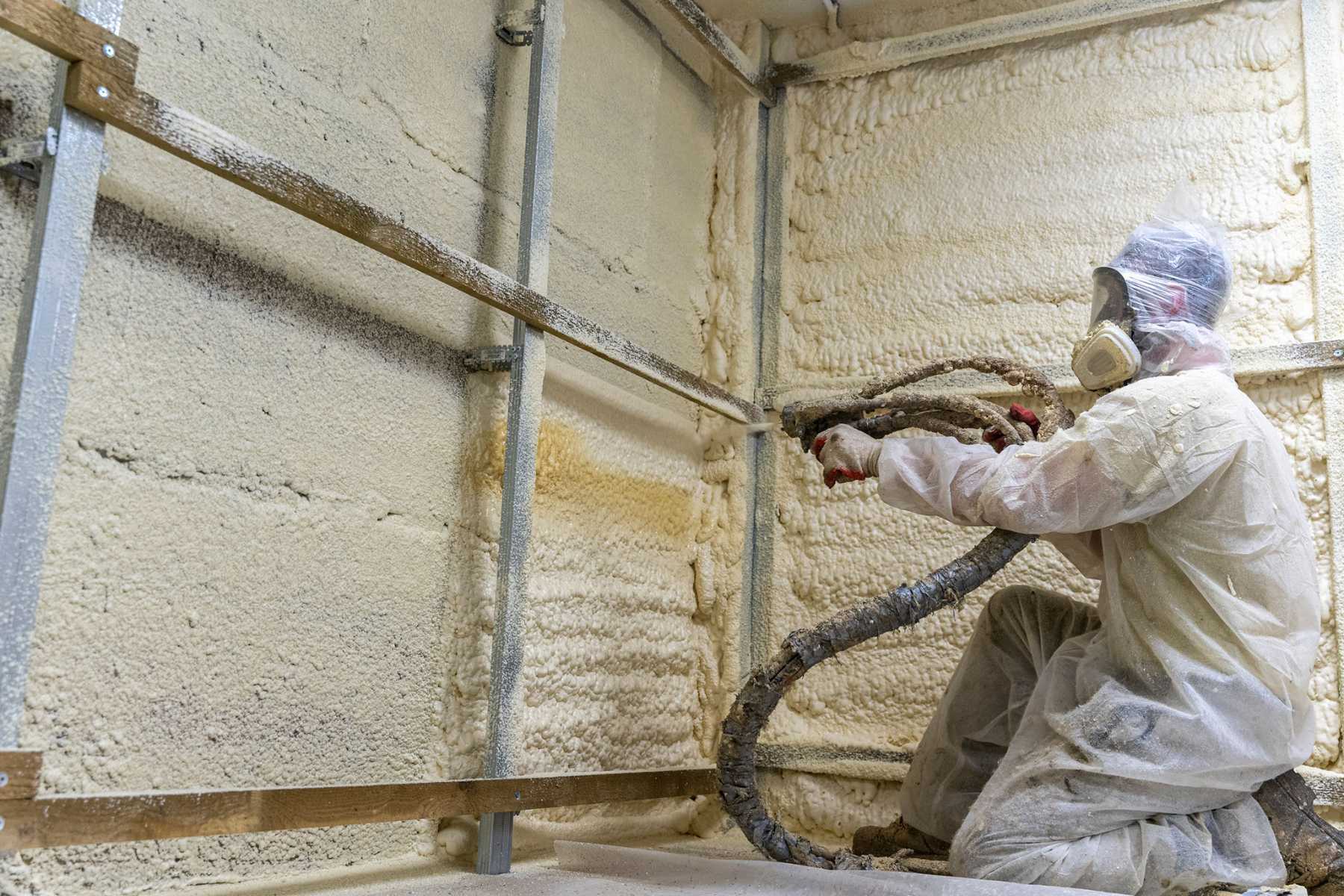 Worker installing spray foam insulation on walls in a metal building.