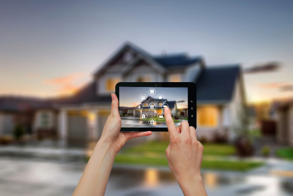 Person using a tablet to control smart home features, with a modern house in the background.